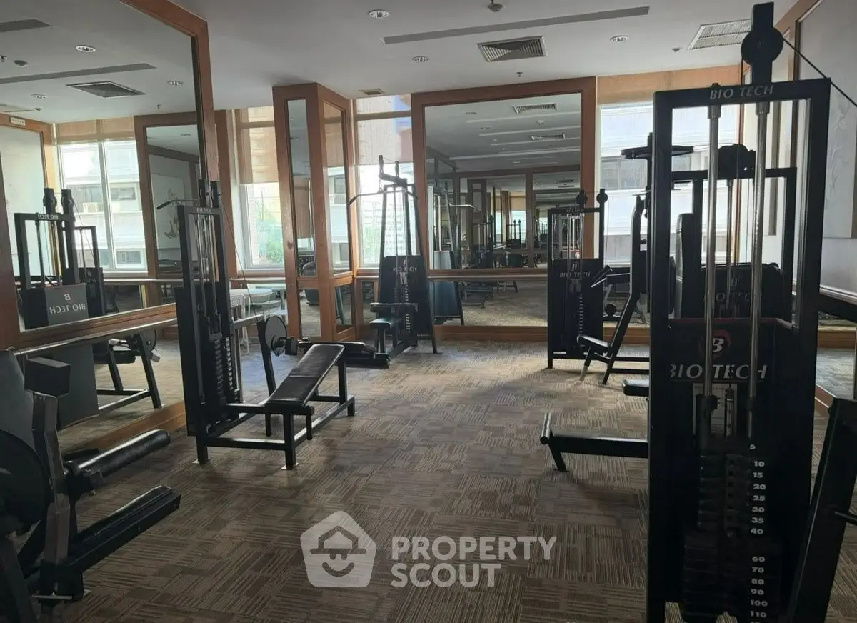 Spacious gym with modern fitness equipment and large mirrors in a residential building.