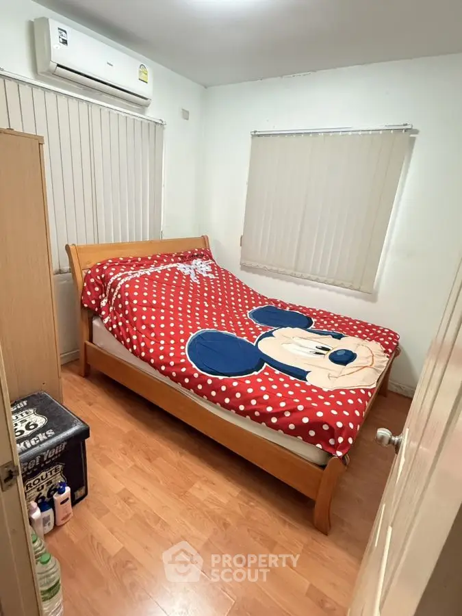Cozy bedroom with wooden flooring and air conditioning, featuring a playful Mickey Mouse bedspread.