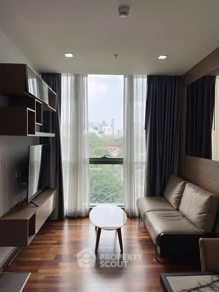 Modern living room with large window and city view, featuring sleek furniture and wooden flooring.