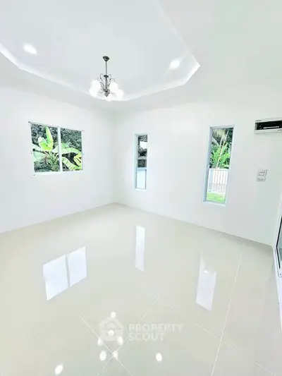 Bright and spacious living room with modern chandelier and large windows overlooking greenery.