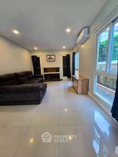 Spacious living room with modern sofa and large windows offering garden view.