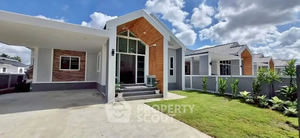 Modern single-story house with large windows and manicured lawn under a bright blue sky.