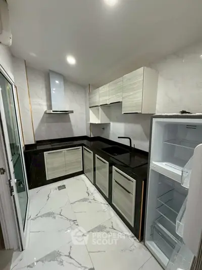 Modern kitchen with sleek black countertops and white cabinets, featuring a built-in fridge and marble flooring.