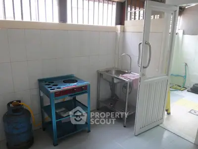 Compact kitchen with gas stove and stainless steel sink in bright tiled room.