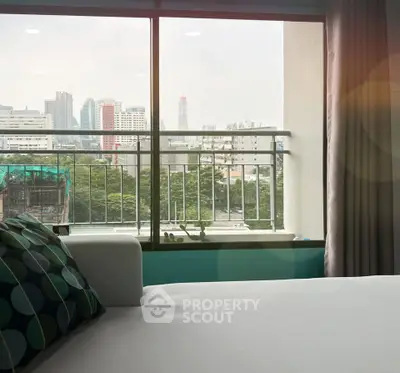 Modern bedroom with city view through large window, featuring stylish decor and comfortable bedding.