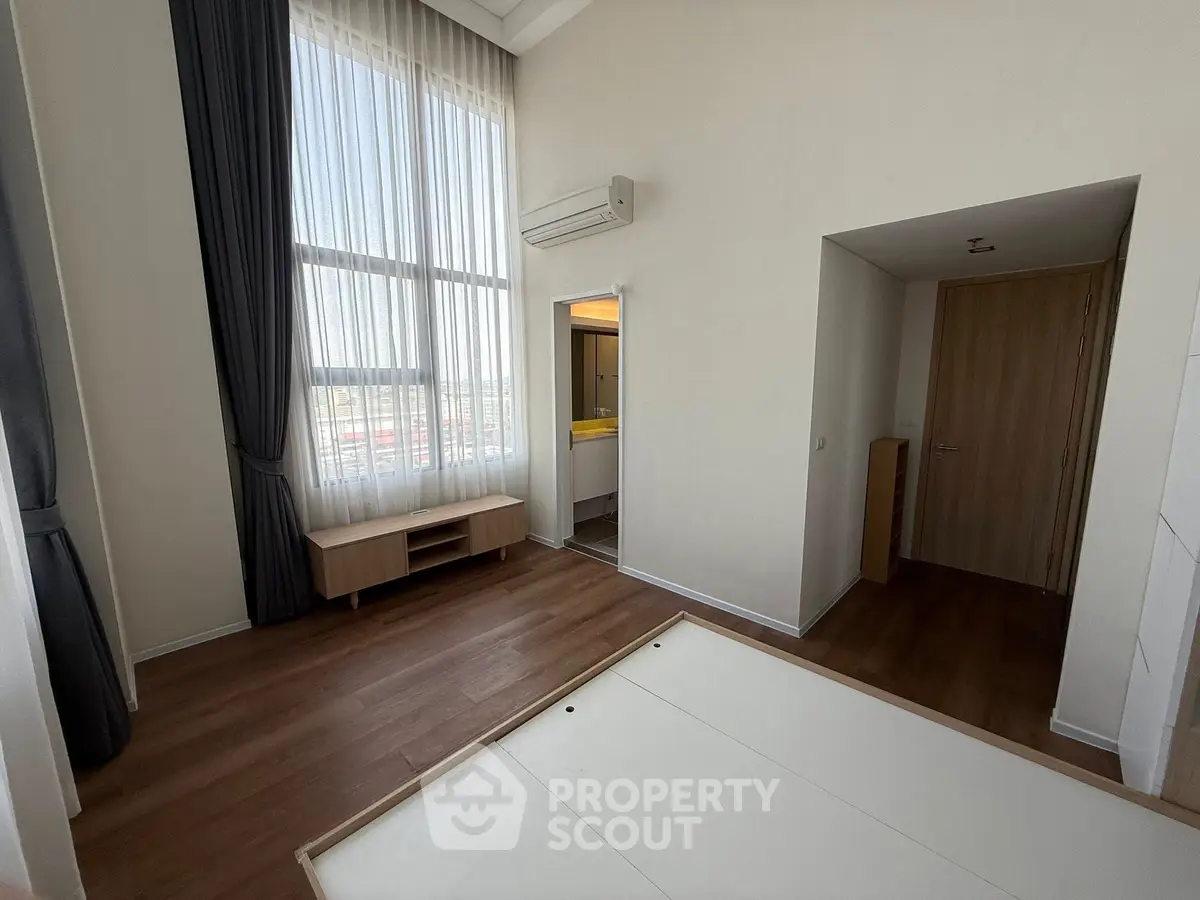 Spacious bedroom with large window and modern design in a high-rise apartment.
