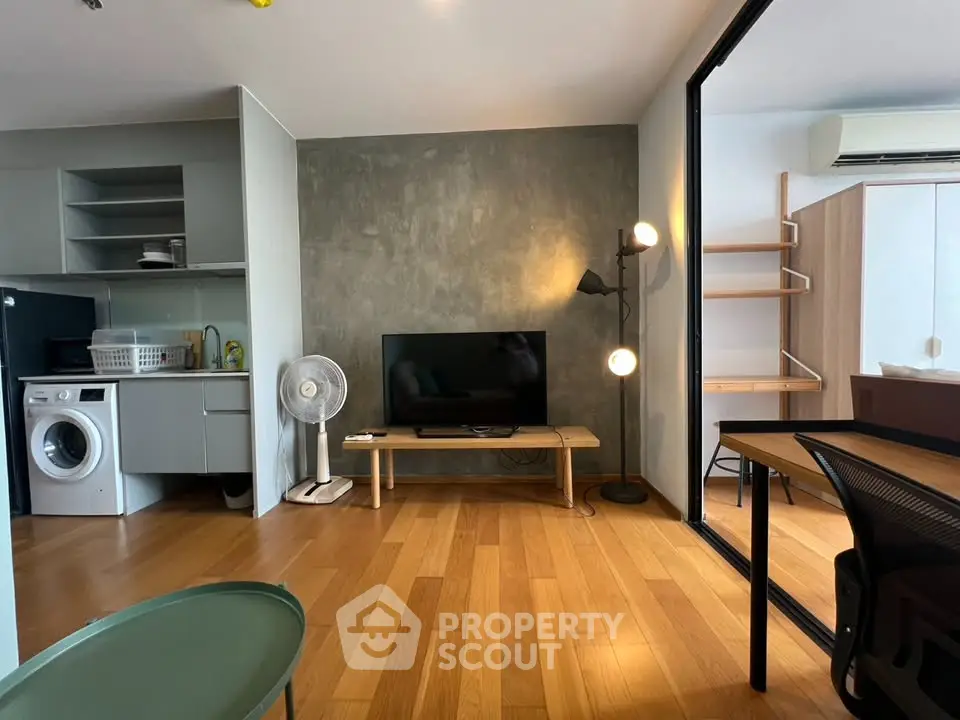 Modern living room with wooden flooring, TV, and washing machine in open layout.