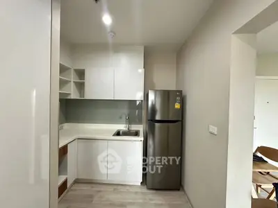 Modern kitchen with sleek white cabinets and stainless steel fridge in cozy apartment.