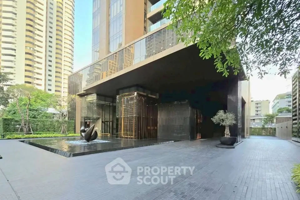 Luxurious modern building entrance with sleek design and water feature in urban setting.