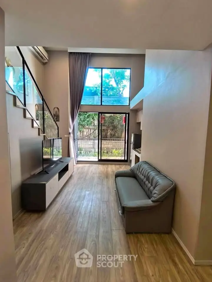 Modern living room with high ceiling and large window, featuring a sleek sofa and TV unit, offering a bright and airy ambiance.