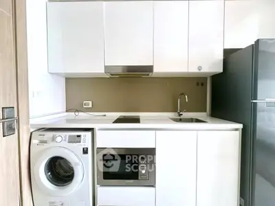 Modern compact kitchen with sleek white cabinets, built-in appliances, and washing machine.