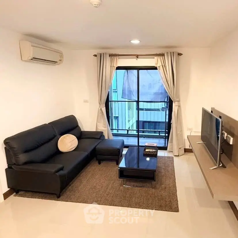 Modern living room with sleek black sofa, wall-mounted TV, and balcony access in a stylish apartment.
