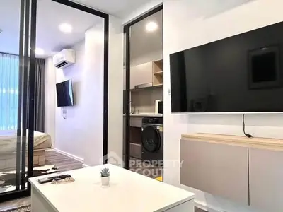 Modern living room with sleek TV setup and view into a compact kitchen area.