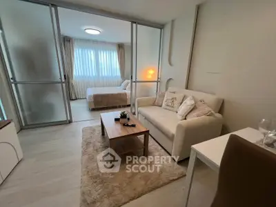 Modern living room with cozy sofa and elegant bedroom separated by glass doors, featuring soft lighting and stylish decor.