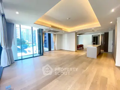 Spacious modern living room with open kitchen and city view, featuring elegant lighting and hardwood floors.