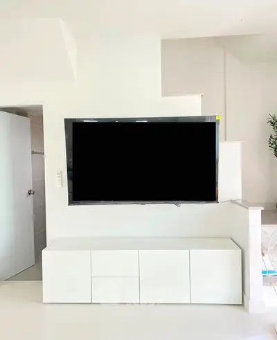 Modern living room with sleek white TV stand and large flat-screen TV, minimalist design.