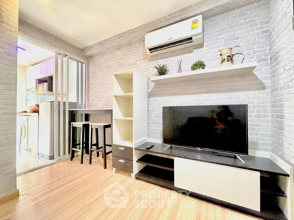 Modern living room with stylish decor and open kitchen layout, featuring air conditioning and sleek TV setup.