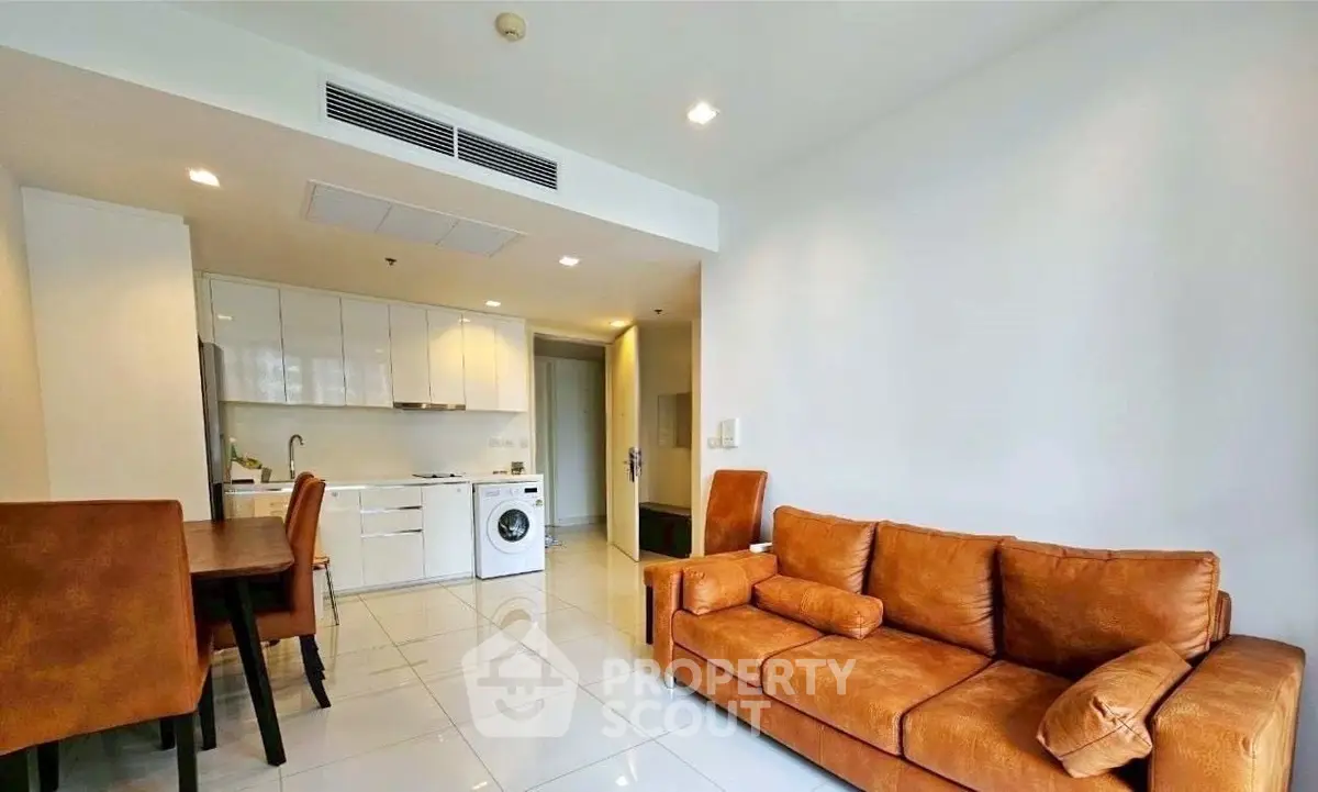 Modern living room with brown leather sofa and open kitchen layout featuring a washing machine.