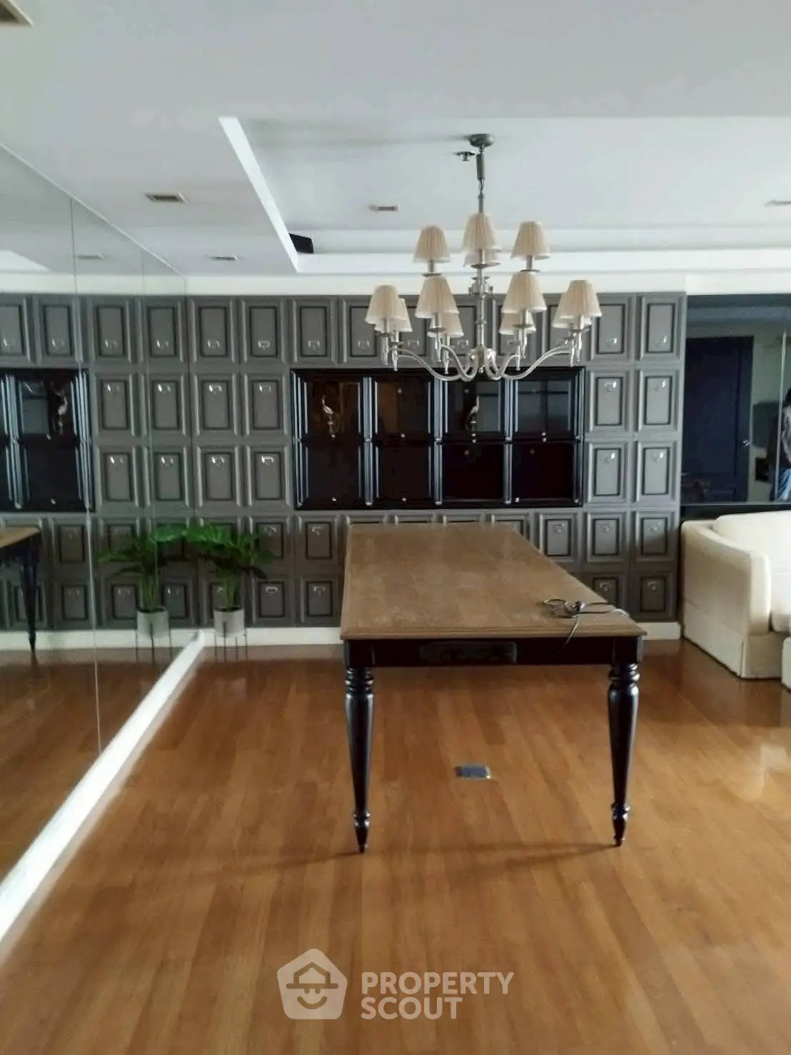 Elegant dining room with wooden table and chandelier, featuring mirrored wall and parquet flooring.