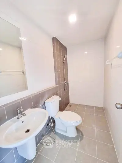 Modern bathroom with sleek fixtures and neutral tiles, featuring a shower and toilet.