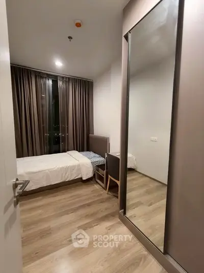 Modern bedroom with sleek design, featuring a single bed, large mirror, and floor-to-ceiling window with curtains.