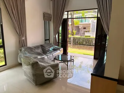 Spacious living room with large windows and garden view, featuring modern furniture and elegant curtains.