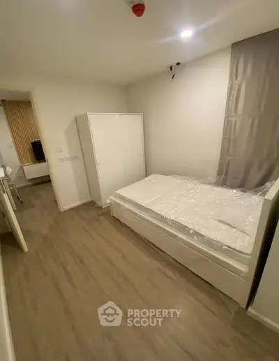 Modern bedroom with wooden flooring and white furniture, featuring a cozy bed and wardrobe.