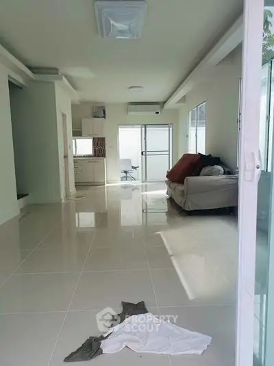 Spacious modern living room with sleek tile flooring and natural light, featuring a cozy sofa and minimalist decor.