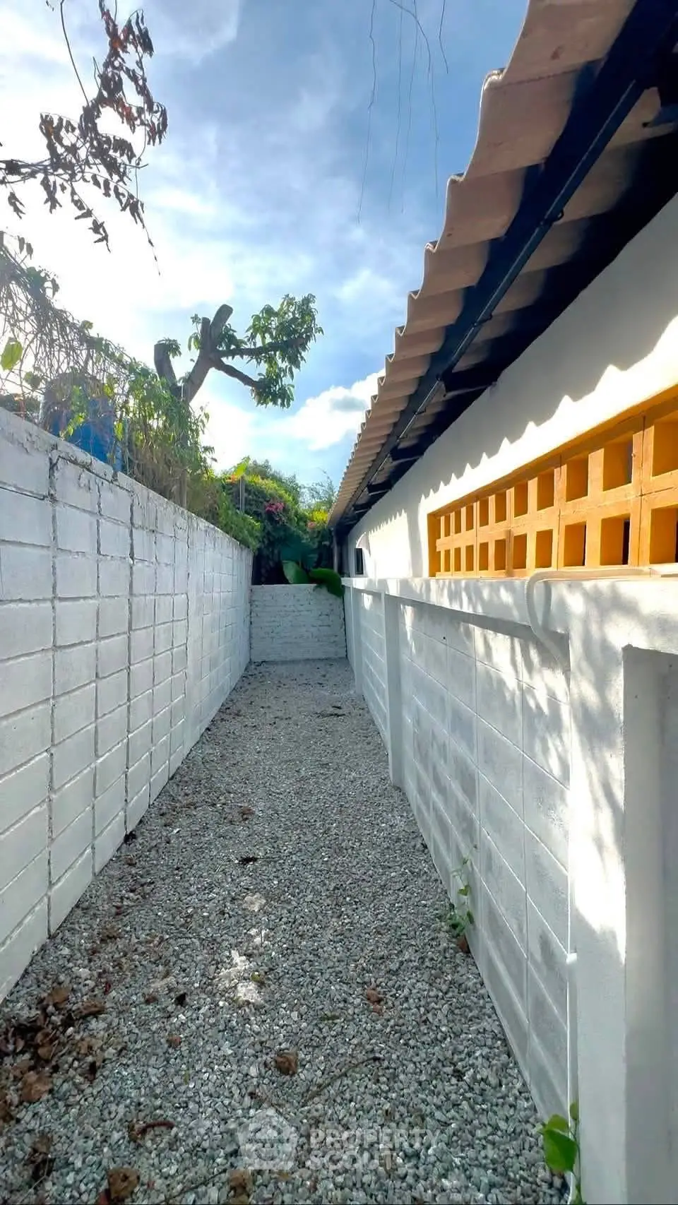 Charming exterior walkway with white brick walls and gravel path, perfect for serene outdoor living.
