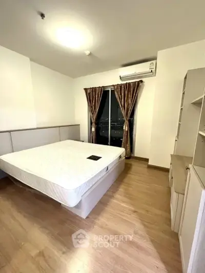 Spacious bedroom with wooden flooring and large window offering city views.