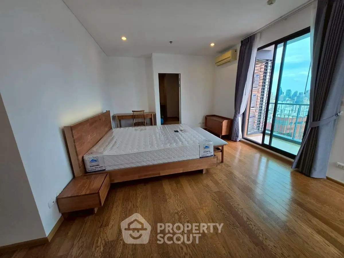 Spacious bedroom with wooden flooring and city view balcony in modern apartment