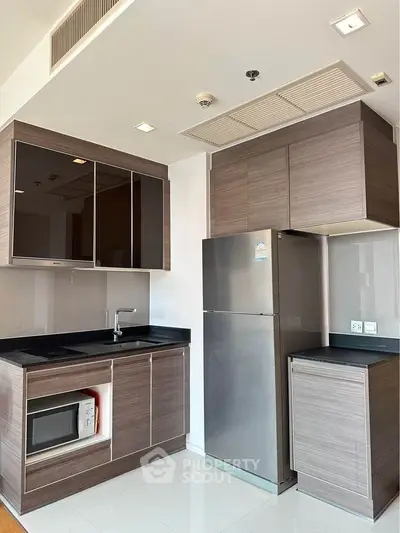 Modern kitchen with sleek cabinetry, stainless steel fridge, and built-in microwave in a stylish apartment.