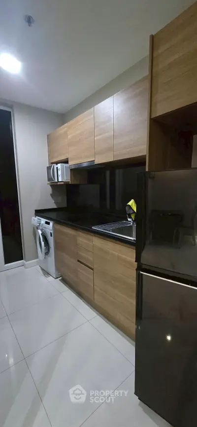 Modern kitchen with wooden cabinets, sleek appliances, and glossy black countertops.