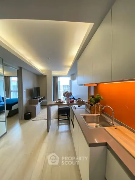 Modern open-layout kitchen and living area with sleek design and vibrant orange backsplash.