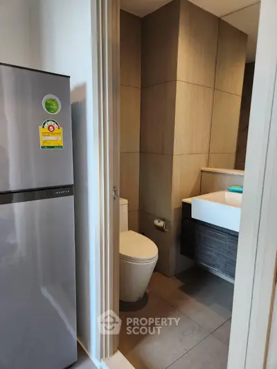 Compact bathroom with modern fixtures next to a sleek refrigerator in a contemporary apartment.