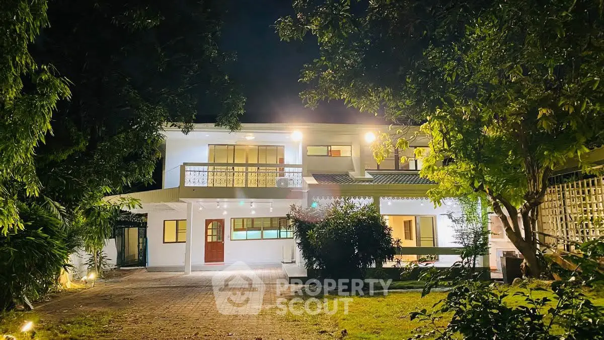 Stunning two-story house with illuminated facade and lush garden at night.