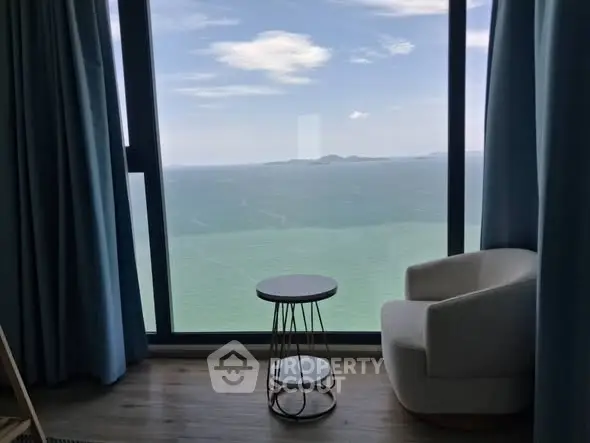 Stunning ocean view from modern high-rise apartment with cozy seating area.