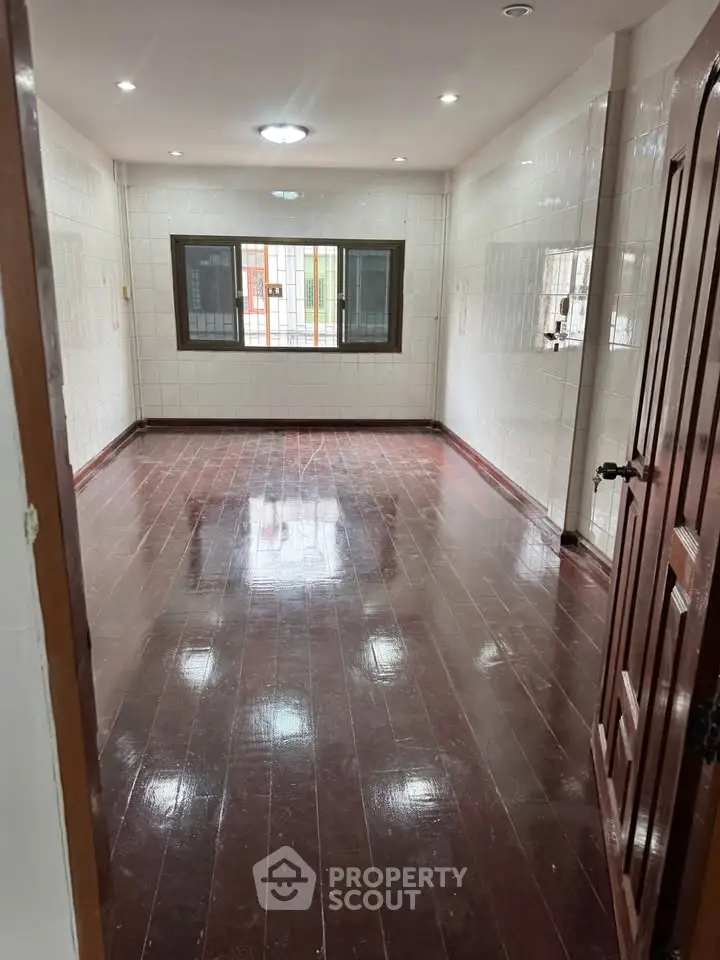 Spacious empty room with glossy wooden floors and large window, ideal for customization.