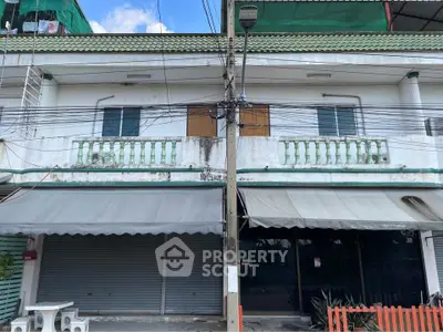 Two-story commercial building with closed shutters and balcony, ideal for business opportunities.