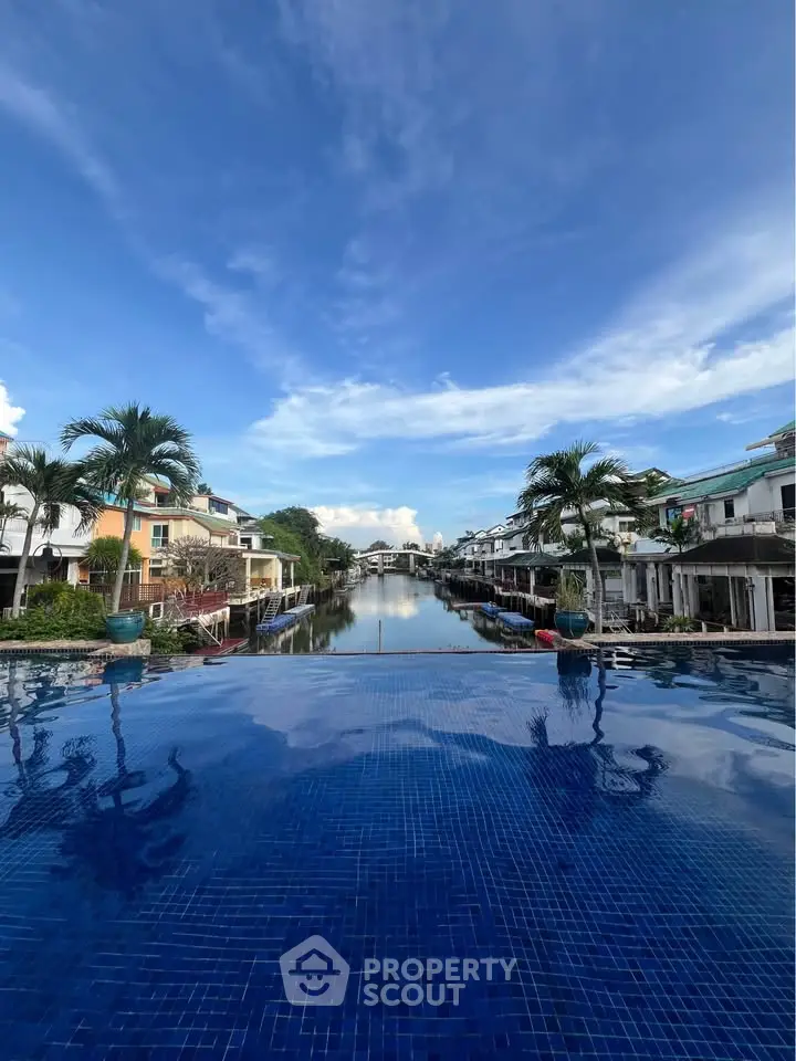 Stunning infinity pool with waterfront view and modern homes under a clear blue sky.