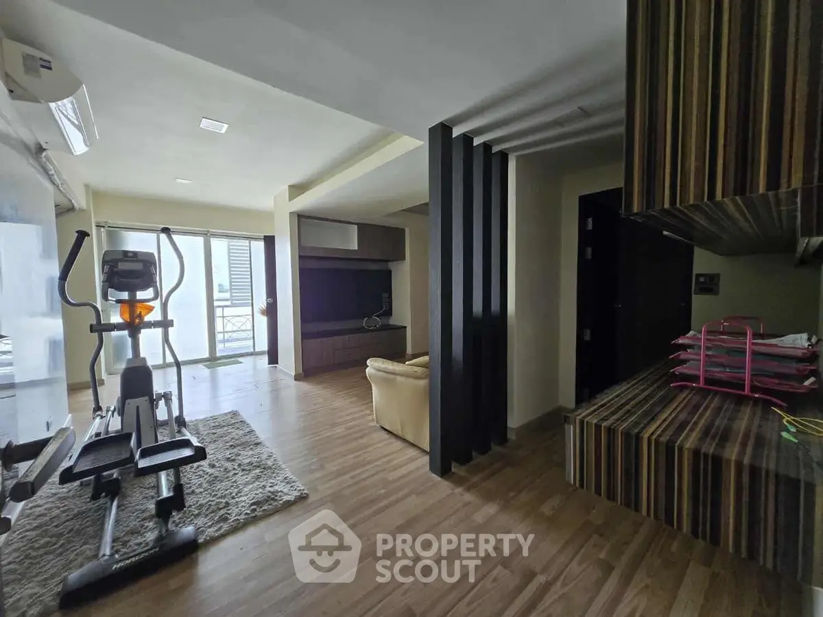 Spacious living room with exercise equipment and modern decor, featuring a large window for natural light.
