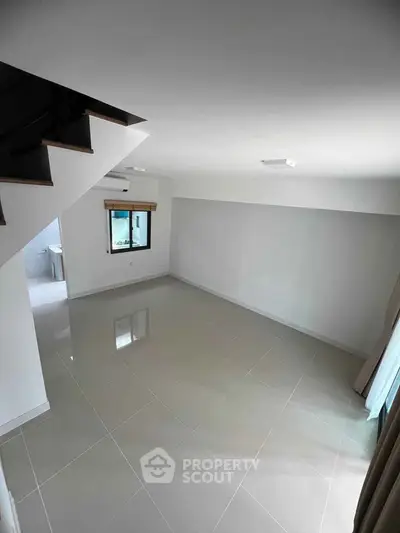 Spacious modern living room with glossy tiled floors and staircase view.