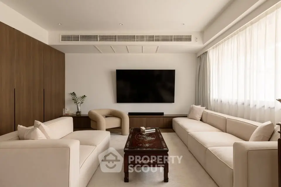 Elegant living room with modern furniture and large TV, featuring a cozy ambiance and natural light.