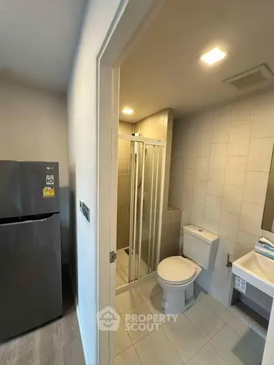 Modern bathroom with shower and adjacent refrigerator in compact apartment setting.