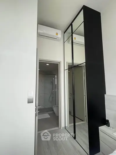 Modern bedroom with mirrored wardrobe and ensuite bathroom in sleek apartment.