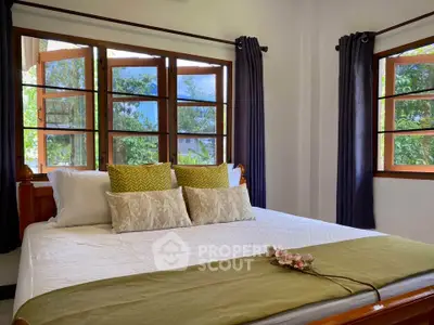 Cozy bedroom with large windows and elegant decor, offering a serene view of lush greenery.