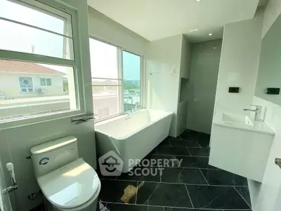 Modern bathroom with large windows and freestanding bathtub offering natural light and views.