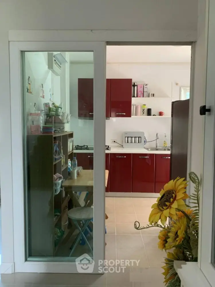 Modern kitchen with red cabinets and glass sliding door, featuring a cozy dining area.
