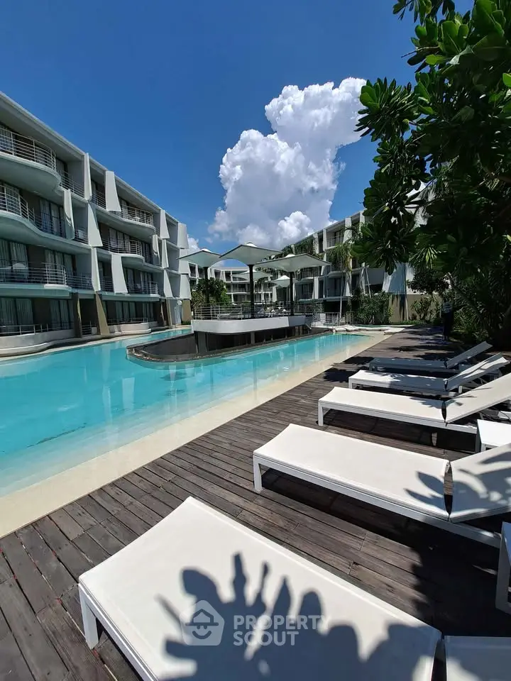Luxurious poolside view at modern apartment complex with sun loungers and clear blue sky.
