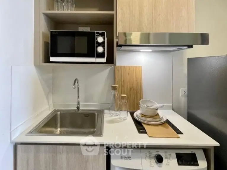 Modern compact kitchen with microwave, sink, and induction cooktop in stylish apartment.